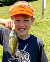 A young boy wearing an orange visor holding up a fish. he caught.